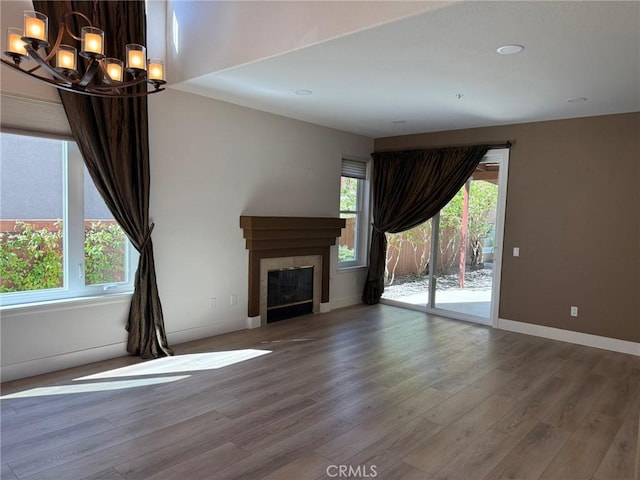 unfurnished living room featuring a glass covered fireplace, a chandelier, plenty of natural light, and wood finished floors