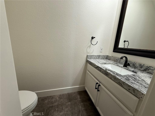 bathroom with baseboards, toilet, vanity, and a textured wall