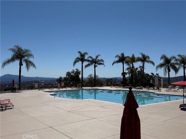 community pool with a mountain view, a patio, and fence