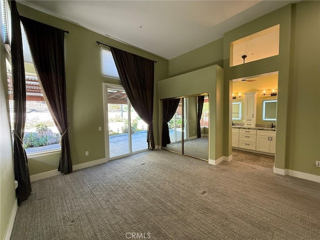 unfurnished bedroom featuring ensuite bath, a towering ceiling, carpet floors, baseboards, and access to exterior