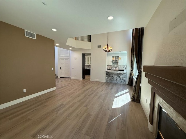 unfurnished living room featuring light wood-type flooring, visible vents, baseboards, and a chandelier