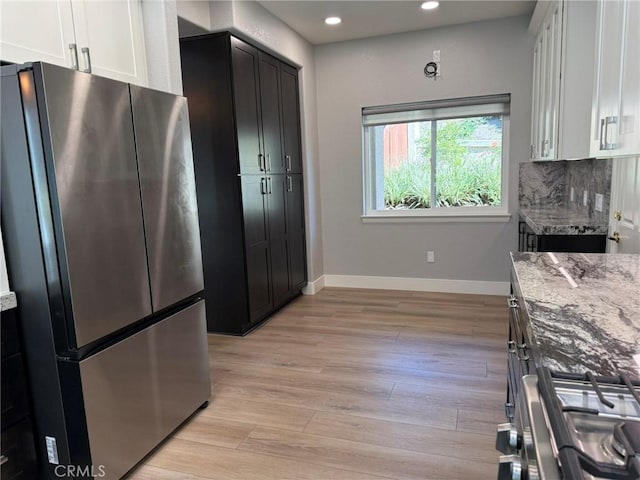 kitchen with light stone counters, light wood-style floors, appliances with stainless steel finishes, decorative backsplash, and baseboards