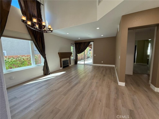 unfurnished living room with an inviting chandelier, a fireplace, baseboards, and light wood-style floors