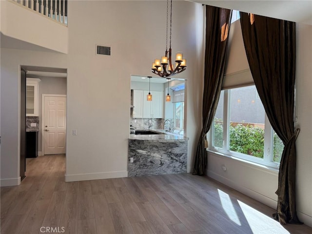 unfurnished dining area featuring a notable chandelier, visible vents, light wood finished floors, and a sink