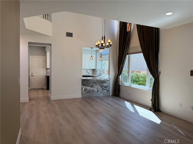 unfurnished dining area with baseboards, visible vents, light wood-style flooring, a towering ceiling, and a chandelier