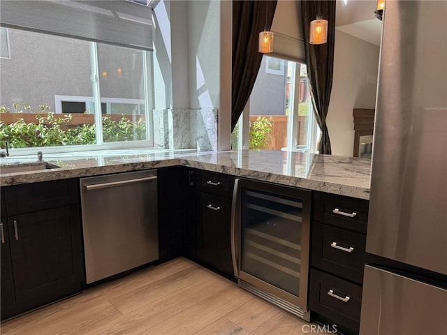 kitchen featuring light stone countertops, beverage cooler, light wood-type flooring, stainless steel appliances, and a sink