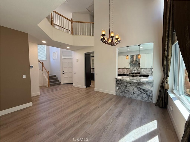 living room featuring stairway, a notable chandelier, light wood-style floors, and baseboards