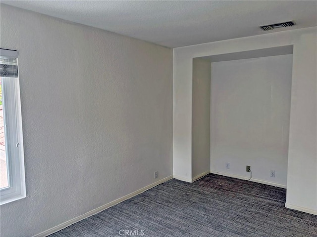 carpeted spare room with visible vents, baseboards, and a textured wall