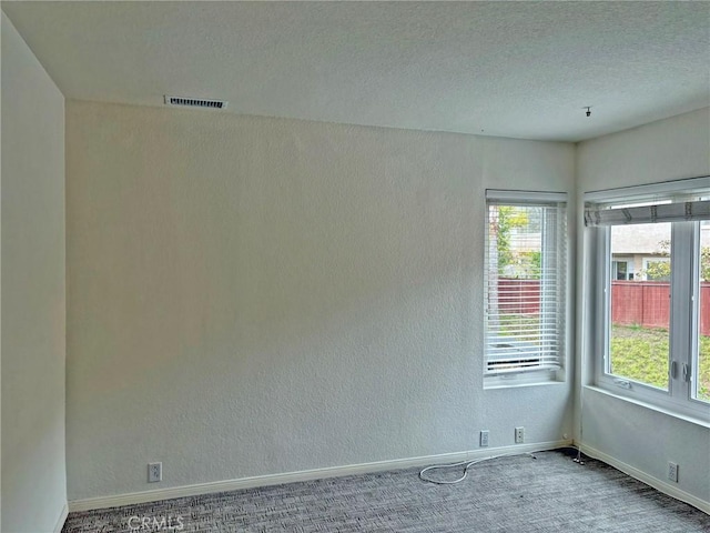 carpeted spare room with visible vents, a textured ceiling, baseboards, and a textured wall