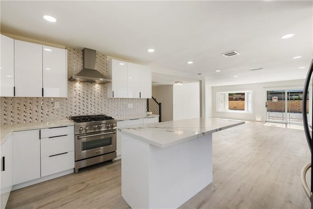 kitchen featuring modern cabinets, high end stainless steel range, backsplash, light wood-style floors, and wall chimney exhaust hood