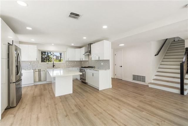 kitchen with wall chimney range hood, visible vents, white cabinets, and stainless steel appliances