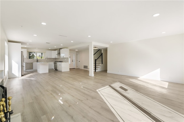 unfurnished living room featuring visible vents, a sink, recessed lighting, light wood finished floors, and stairs