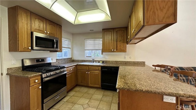 kitchen with a kitchen bar, brown cabinets, appliances with stainless steel finishes, a peninsula, and a sink