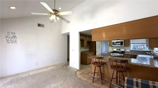 kitchen featuring visible vents, a peninsula, a sink, appliances with stainless steel finishes, and light colored carpet