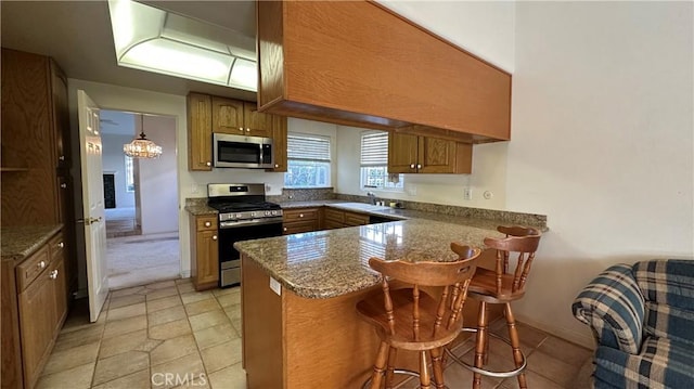 kitchen with a kitchen breakfast bar, appliances with stainless steel finishes, a peninsula, brown cabinetry, and a sink