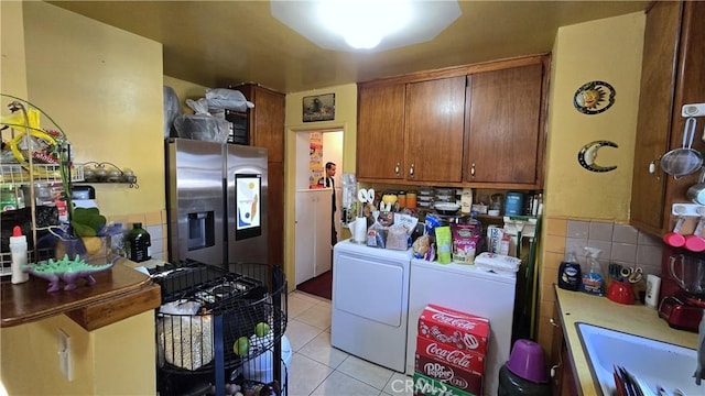 kitchen with brown cabinets, washer and clothes dryer, light tile patterned floors, a sink, and stainless steel fridge