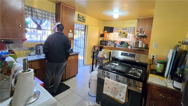 kitchen featuring brown cabinetry, gas stove, light countertops, and light tile patterned floors