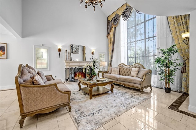 living room with a warm lit fireplace, a notable chandelier, a towering ceiling, and baseboards