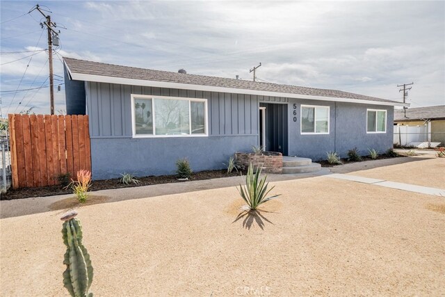 ranch-style home with board and batten siding, fence, and a shingled roof