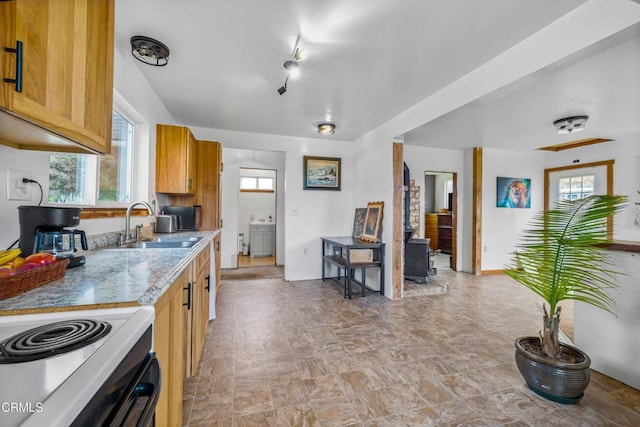 kitchen with electric stove, a sink, washer / dryer, and brown cabinets