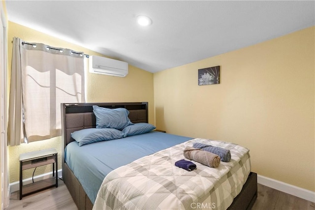 bedroom featuring wood finished floors, baseboards, and a wall mounted AC