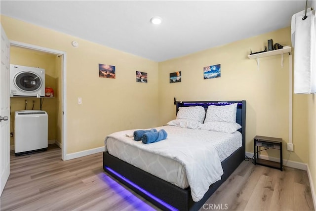 bedroom with stacked washing maching and dryer, baseboards, and light wood-style floors