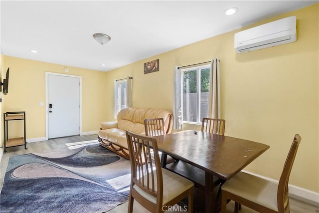 dining space with an AC wall unit, light wood-style floors, recessed lighting, and baseboards