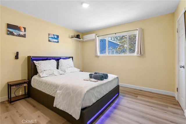 bedroom featuring a wall unit AC, wood finished floors, and baseboards