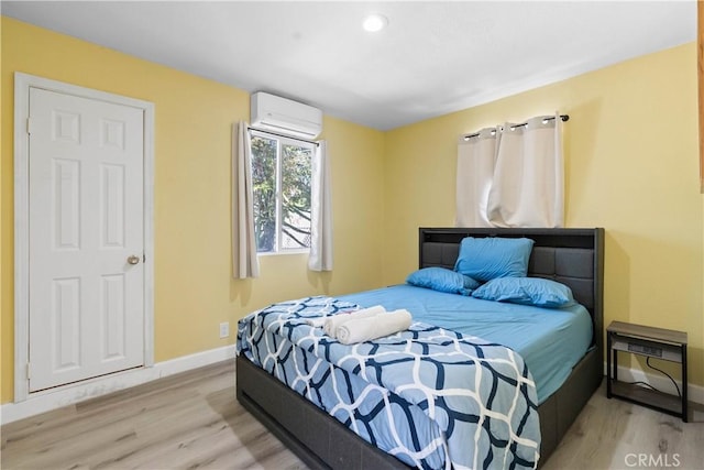 bedroom featuring baseboards, wood finished floors, and a wall mounted AC