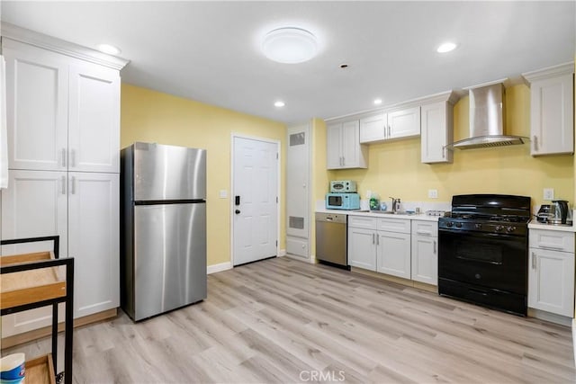 kitchen featuring light wood finished floors, wall chimney exhaust hood, stainless steel appliances, light countertops, and a sink