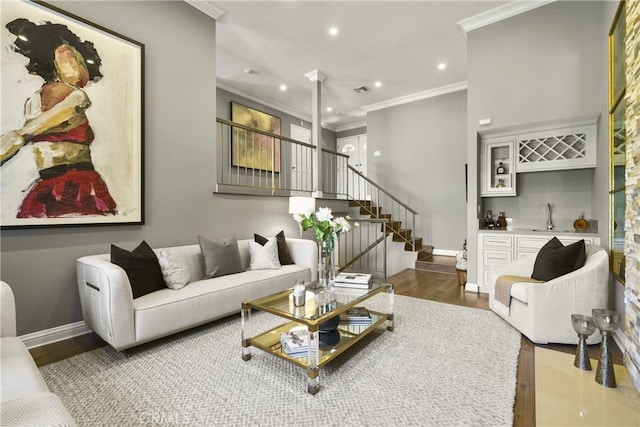 living room featuring stairs, crown molding, wood finished floors, and wet bar