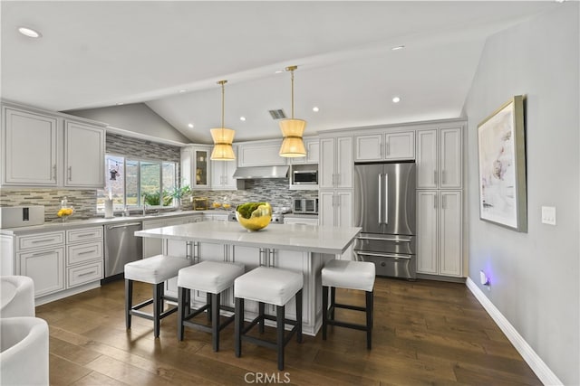 kitchen with dark wood-style floors, stainless steel appliances, lofted ceiling, light countertops, and a kitchen breakfast bar