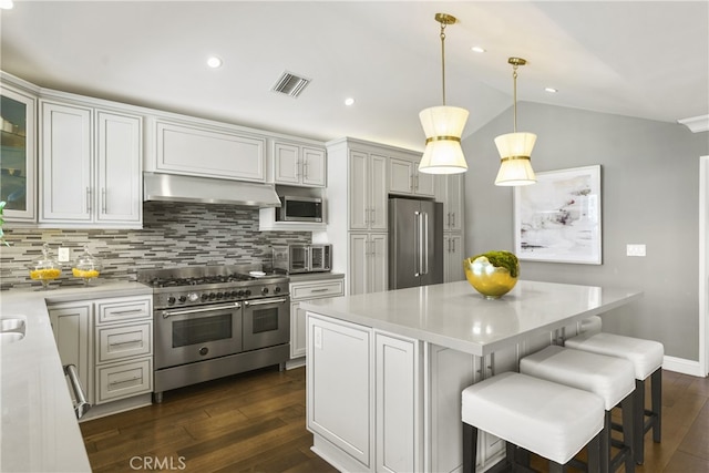 kitchen with visible vents, premium appliances, wall chimney exhaust hood, vaulted ceiling, and light countertops