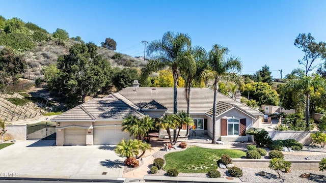 ranch-style home with a tile roof, a chimney, stucco siding, a garage, and driveway