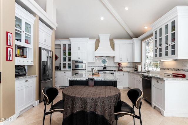 kitchen featuring tasteful backsplash, lofted ceiling, custom range hood, stainless steel appliances, and a sink