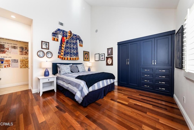 bedroom featuring dark wood finished floors, a towering ceiling, and baseboards