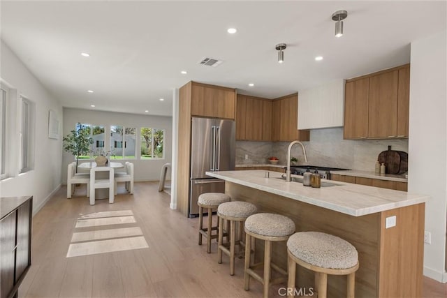 kitchen with visible vents, a breakfast bar, brown cabinets, high end fridge, and a sink