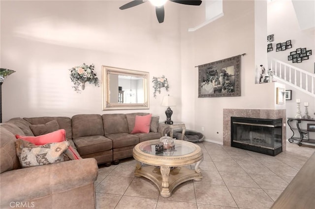 living area with a tile fireplace, ceiling fan, tile patterned floors, stairs, and a high ceiling