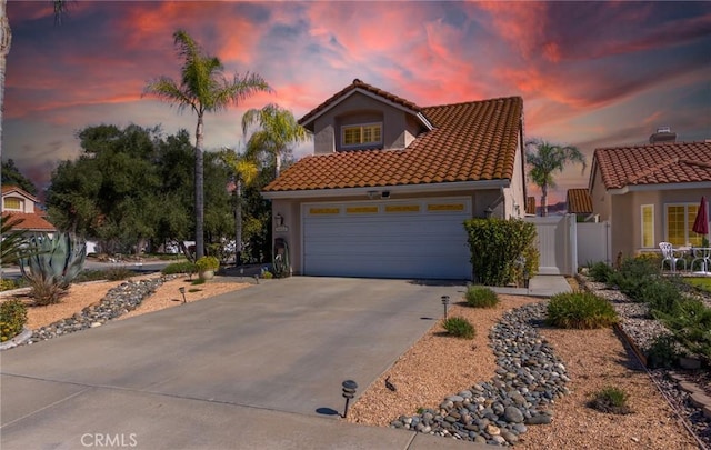 mediterranean / spanish-style house featuring an attached garage, fence, a tiled roof, driveway, and stucco siding