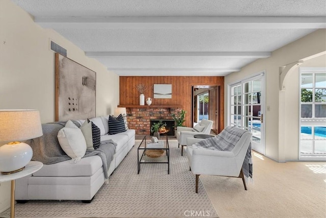 living area featuring a fireplace, beamed ceiling, a textured ceiling, and light colored carpet