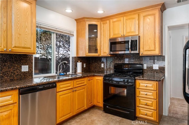 kitchen featuring backsplash, appliances with stainless steel finishes, glass insert cabinets, a sink, and dark stone counters