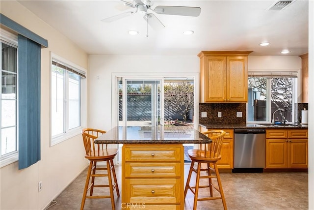 kitchen featuring a breakfast bar area, dark stone counters, a sink, backsplash, and dishwasher