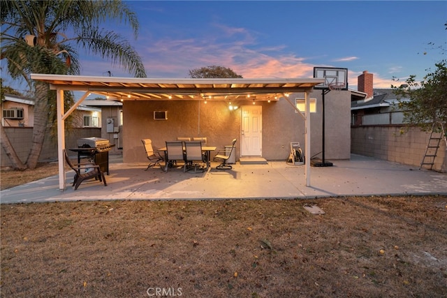 back of property at dusk featuring a patio, fence, and stucco siding