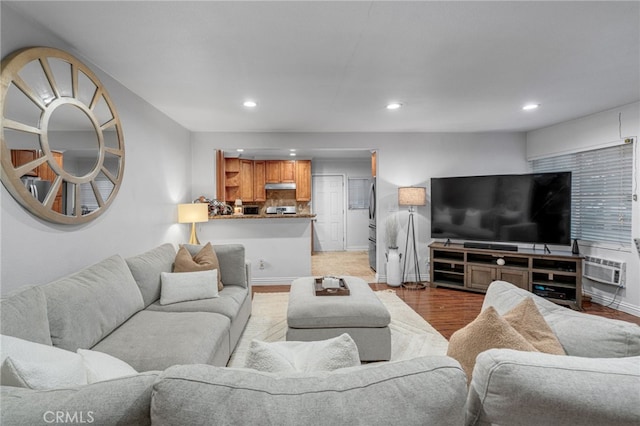 living room featuring light wood-style flooring, a wall mounted air conditioner, baseboards, and recessed lighting