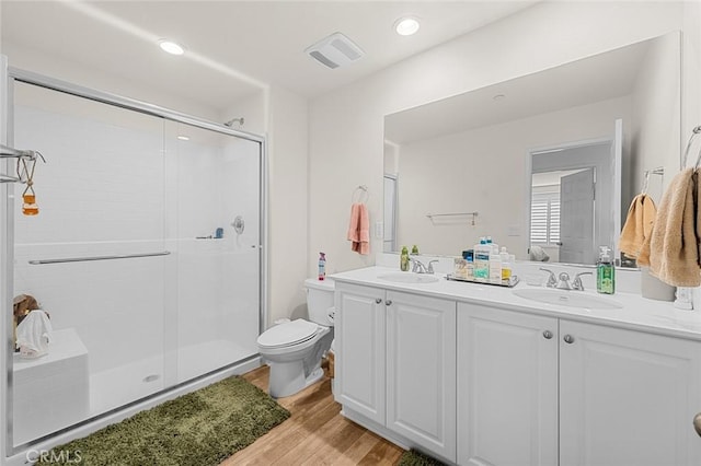 full bathroom with double vanity, visible vents, a stall shower, a sink, and wood finished floors