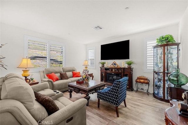 living room featuring a glass covered fireplace, a healthy amount of sunlight, visible vents, and light wood-style flooring