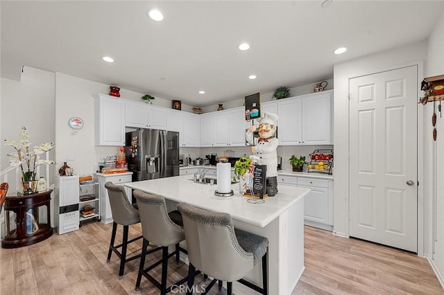 kitchen featuring light wood-type flooring, fridge with ice dispenser, an island with sink, and a kitchen bar