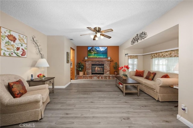 living area featuring a brick fireplace, a textured ceiling, baseboards, and wood finished floors