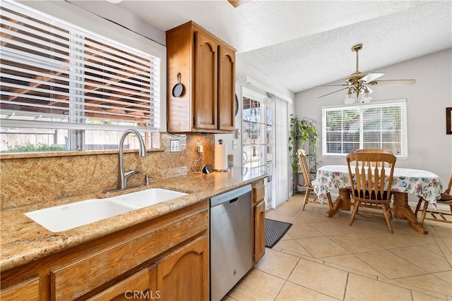 kitchen featuring brown cabinetry, vaulted ceiling, a sink, and stainless steel dishwasher