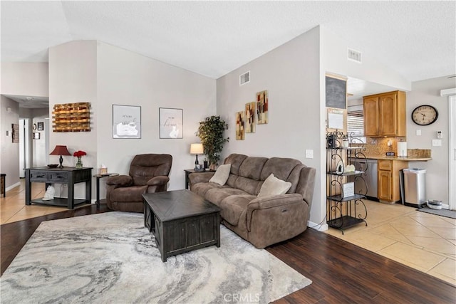 living area featuring visible vents, vaulted ceiling, and light wood-style flooring